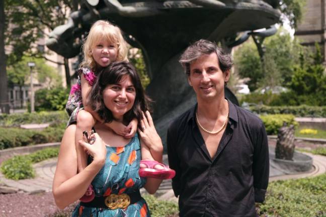 The co-founders of Kimera Festival: Athena Azevedo, executive director of IBOC (left) and Joao MacDowell, artistic director of IBOC (right), with their daughter in front of the Peace Fountain Chimera sculpture, located at 1047 Amsterdam Avenue. Photo: Beau Matic.