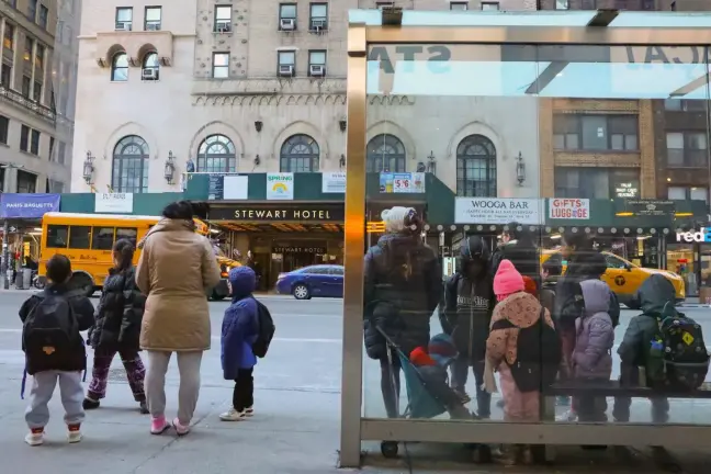 A group of migrant students waits for a bus across from the Stewart Hotel shelter in Midtown on the way to school, Jan. 24, 2025.