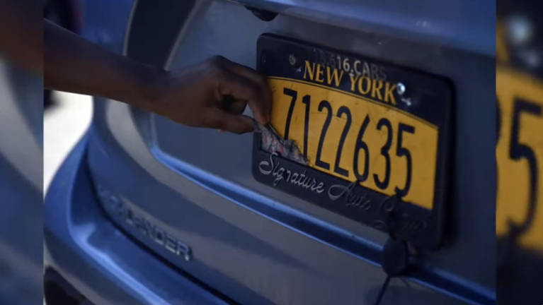 A law enforcement official pulls a strip of paper off a plate which rendered the license unreadable by toll scanners. Manhattan borough president Mark Levine says one in 20 drivers are using so called ghost plates.