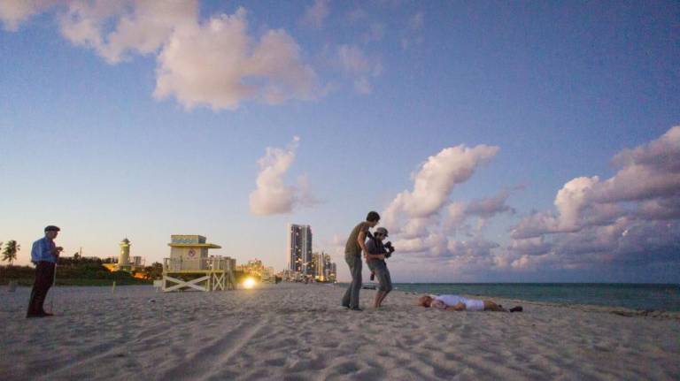 Production still from “<i>Noogie’s Time To Shine</i>:” Jim Knipfel, with his white blind person’s cane, at left. The movie’s titular star, Brandon Potter is prostate on the beach right.